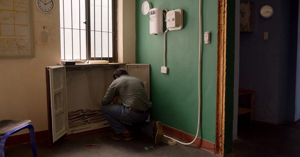 An electrician working at an open electrical panel inside an Indian building
