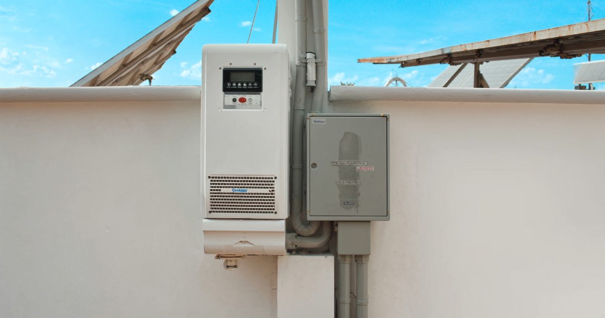 A solar inverter and distribution box mounted on the wall of an Indian home, with rooftop panels above
