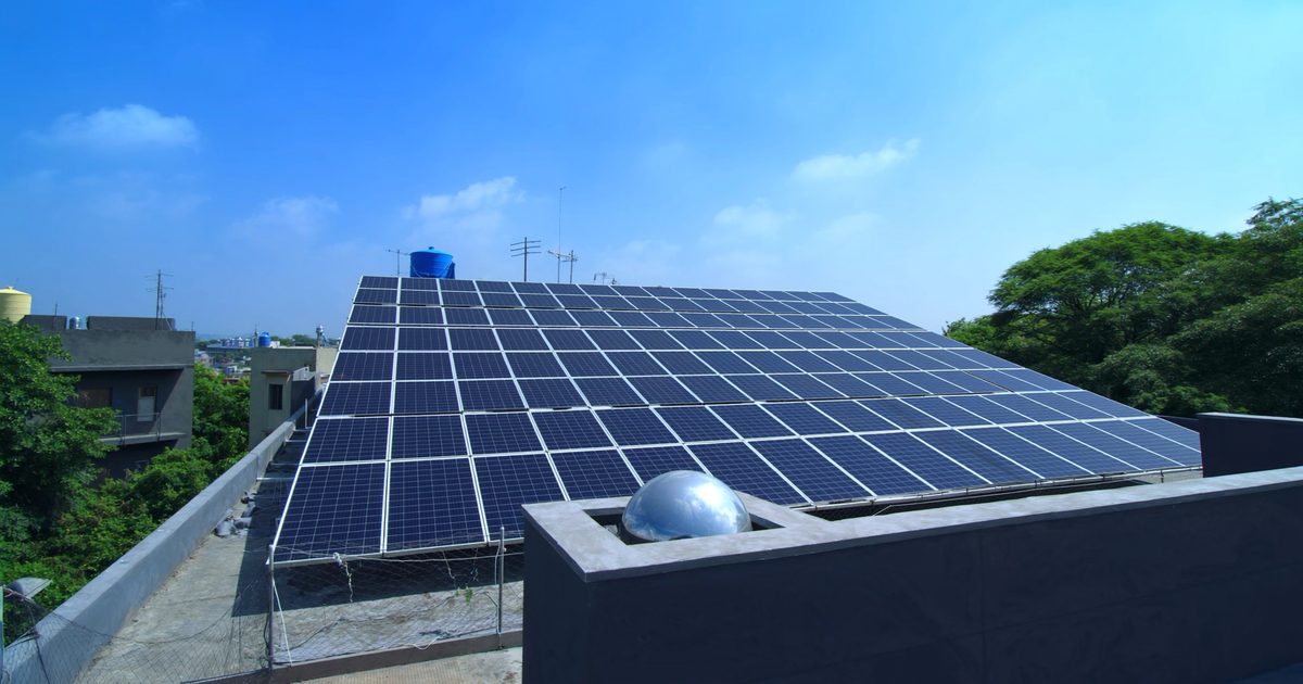 Rooftop solar panel array on an Indian home under a clear midday sky